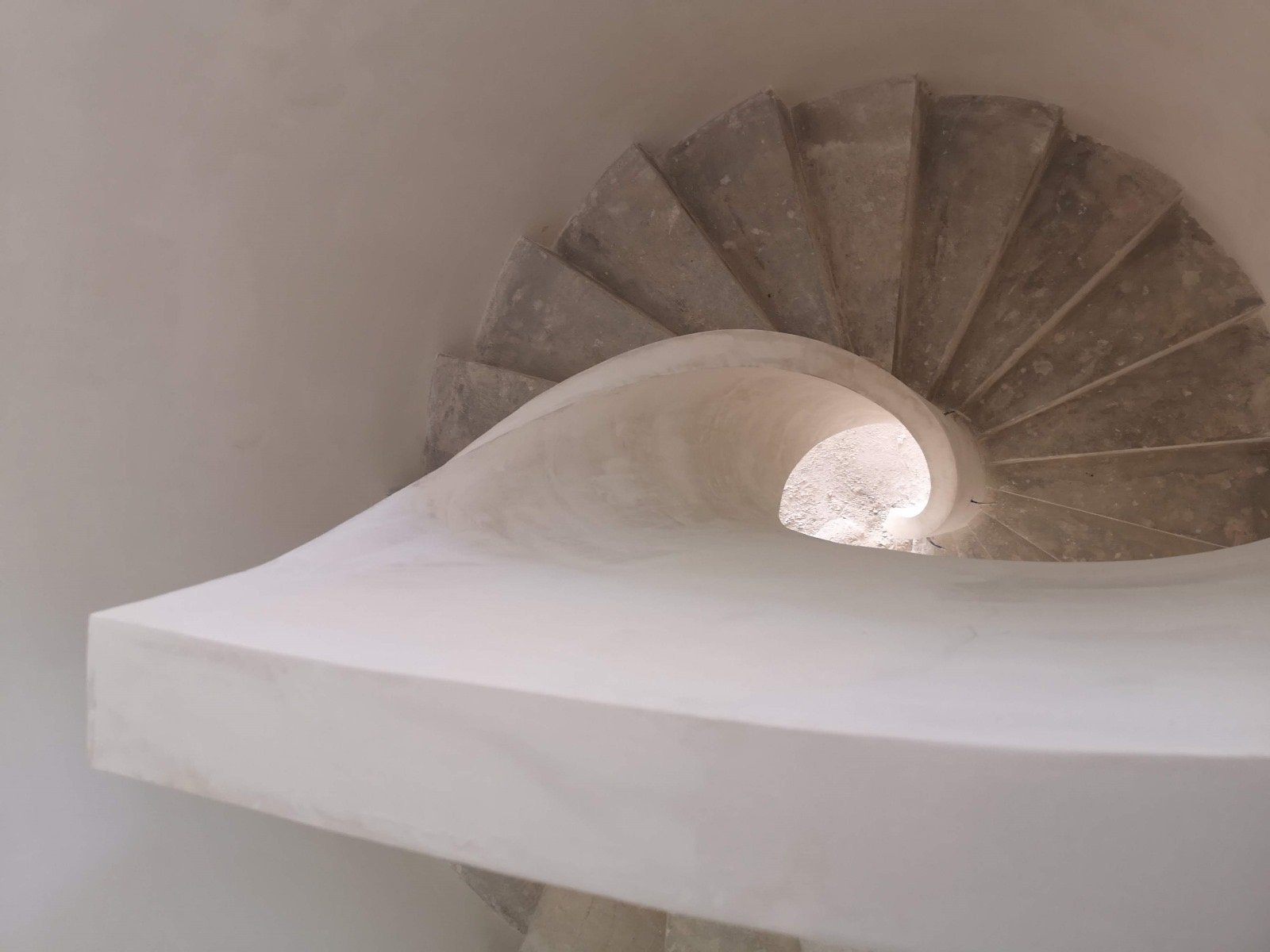 Vista en espiral desde arriba de una escalera de caracol de hormigón con acabado blanco, destacando el diseño curvo de la barandilla.