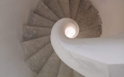 Vista cenital de una escalera de caracol de hormigón con barandilla blanca lisa, en espiral descendente.