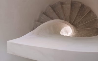 Vista en espiral desde arriba de una escalera de caracol de hormigón con acabado blanco, destacando el diseño curvo de la barandilla.