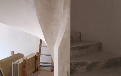 Escalera de caracol completamente enlucida con acabado liso blanco, en el interior de un edificio en construcción.
